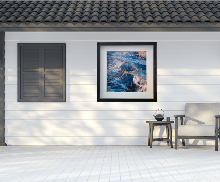 Framed abstract art on a white wall with a chair and small table below.