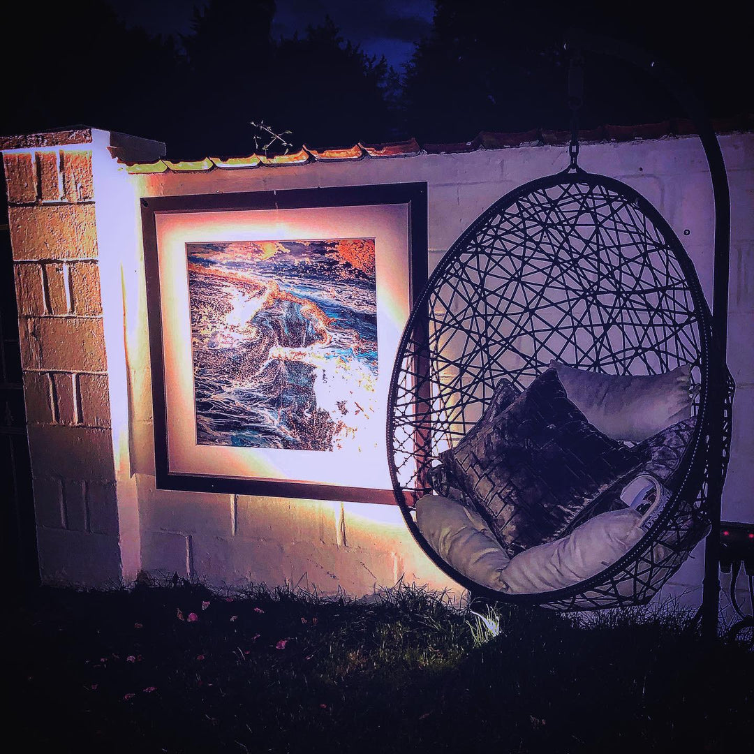 Hanging chair with cushions next to an outdoor framed artwork on a wall at night.