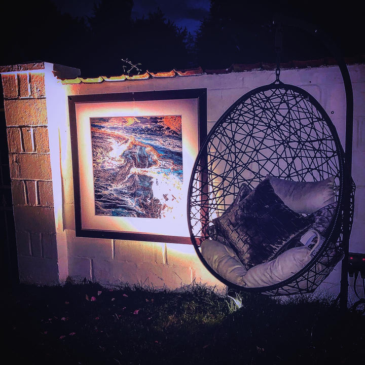 Hanging chair with cushions next to an outdoor framed artwork on a wall at night.